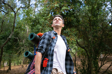 Hiking man looking at nature landscape. Attractive Caucasian young tourist with backpack enjoying scenery and walking in forest. Backpacking tourism, adventure and summer vacation concept