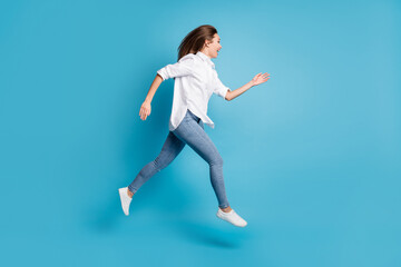 Fototapeta na wymiar Full length profile photo of lady jumping high up running wear white shirt jeans shoes isolated blue color background