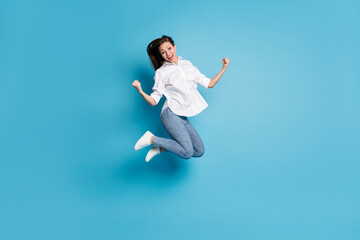 Full body photo of crazy lady jump high up raise fists victory wear white shirt jeans shoes isolated blue color background