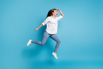 Fototapeta na wymiar Full length photo lady jump high running look far away interested wear white shirt jeans shoes isolated blue color background
