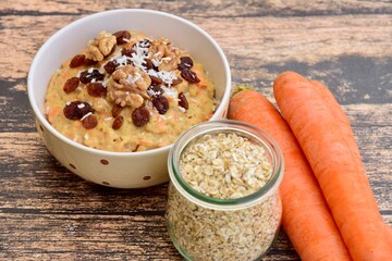 Carrot oat porridge with raisin, walnut and coconut flakes. Wooden background