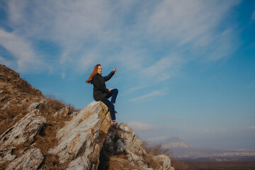 Fototapeta premium A young woman sits high on a mountain against a blue sky.