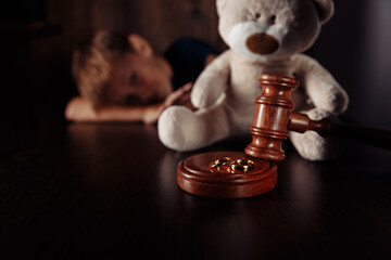 Divorce and separation concept. Wooden gavel, rings and frustrated boy with teddy bear. Family law.