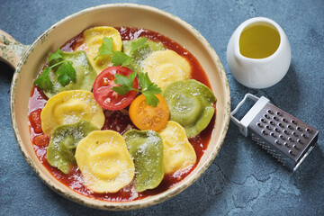 Ravioli with tomato sauce and grated parmesan in a beige serving pan, studio shot on a blue stone surface