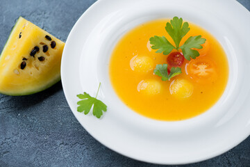 Yellow tomatoes and yellow watermelon gazpacho served in a white plate, studio shot on a blue stone background