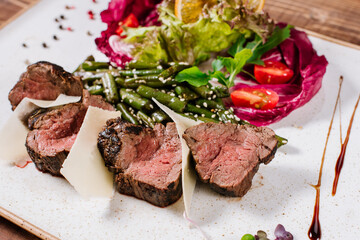 Medium rare meat medalions with vegetables on wooden background