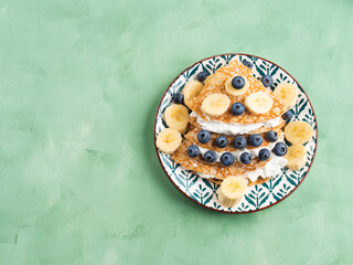 Christmas tree shaped sweet crepes with cream greek yogurt filling and blueberry topping on pastel green table.