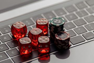 Online casino concept. Gambling chips and five red dices on laptop keyboard close-up.