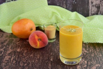 Fresh mango peach smoothie with hemp seeds and maca powder on wooden background