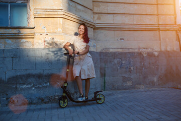 Happy pretty lady in dress with scooter. Sun light on facade of building. Active leisure and new place idea, copy space