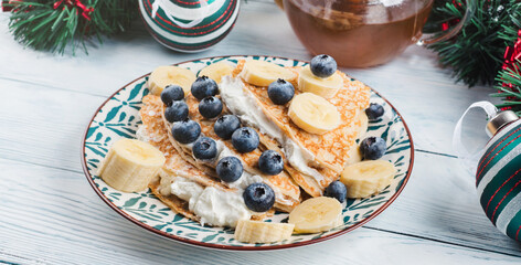 Christmas tree shaped sweet crepes filled with cream greek yogurt, banana and blueberries on white...