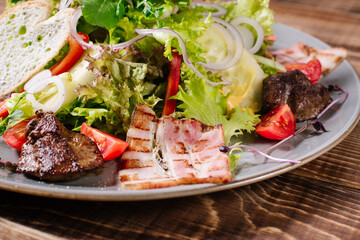 A salad of grilled meat, bacon and vegetables on wooden background