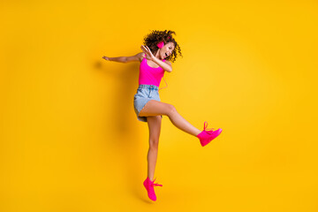 Fototapeta na wymiar Full body profile photo of charming crazy lady jump high carefree listen earphones modern technology dancing dab wear pink tank top mini skirt shoes isolated bright yellow color background