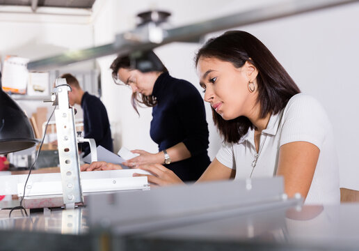 Young female architect working on fret saw, creating details for new architectural model in design bureau