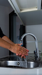 A Caucasian man washes his hands in the kitchen of his house
