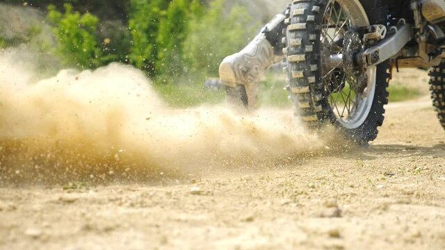 Close up wheel of powerful off-road motorcycle starting movement and kicking up dry ground or dust. Motocross bike starts movement. Concept of motorsport or active lifestyle. Slow motion Back view