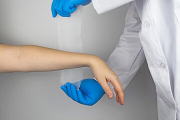 The traumatologist puts a bandage on the forearm of the female patient. The concept of help with fractures and sprains. The technique of applying a cruciform bandage.