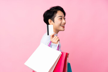 Young Asian girl over isolated pink background holding shopping bags and a credit card