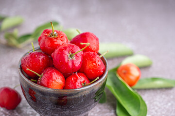 Ripe red cherries in a ceramic bowl with leaves on stone background. Space for text. Sweet organic berries. Concept of healthy fruits