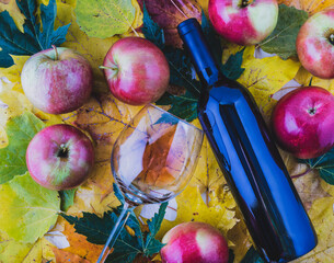 Red and ripe apples in a wicker basket with maple leaves.A bottle of wine and a thin-stemmed glass.