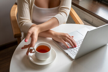 Lonely woman freelancer enjoying having breakfast with cup of coffee working on laptop sitting near window in cafe at morning. View on bust of female
