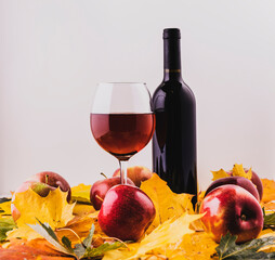 Red and ripe apples in a wicker basket with maple leaves.A bottle of wine and a thin-stemmed glass. - 386899612