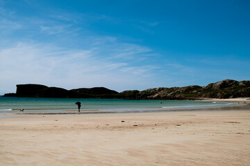 Oldshoremore beach, Scotland with silhouette of man with umbrella and dog