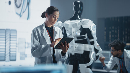 In Development Laboratory: Portrait of a Beautiful Chief Female Engineer Using Digital Tablet Computer. Scientists Work on Prototype Exoskeleton Designed to Help Disabled People, Hard Labor Workers