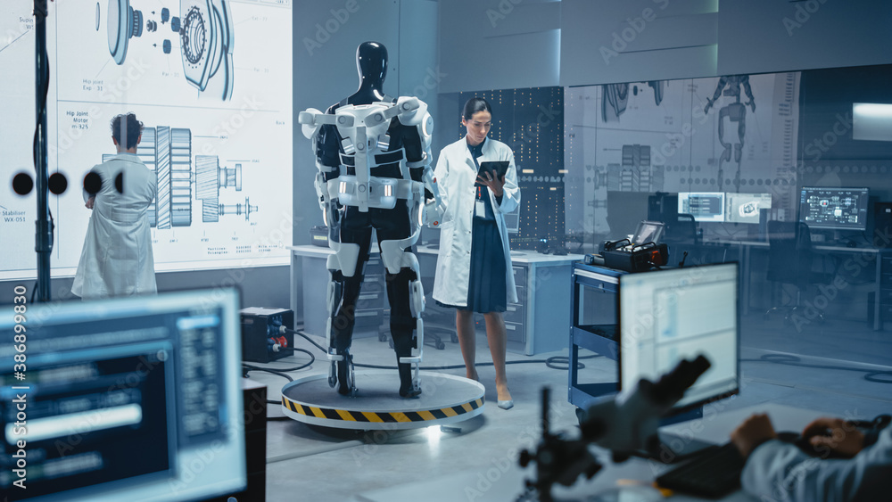 Leinwandbilder In Robotics Development Laboratory: Female Scientist Uses Digital Tablet Computer, Work on a Robotics Exoskeleton Prototype. Engineers Designing Exosuit to Help Disabled People, Workers Lift Goods 