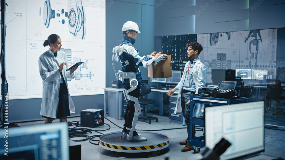 Fototapete In Development Laboratory: Engineers Work on a Robotic Exoskeleton with a Person Testing it by Holding Heavy Cardboard Box. Designing Wearable Exosuit to Help Hard Labor Warehouse Workers