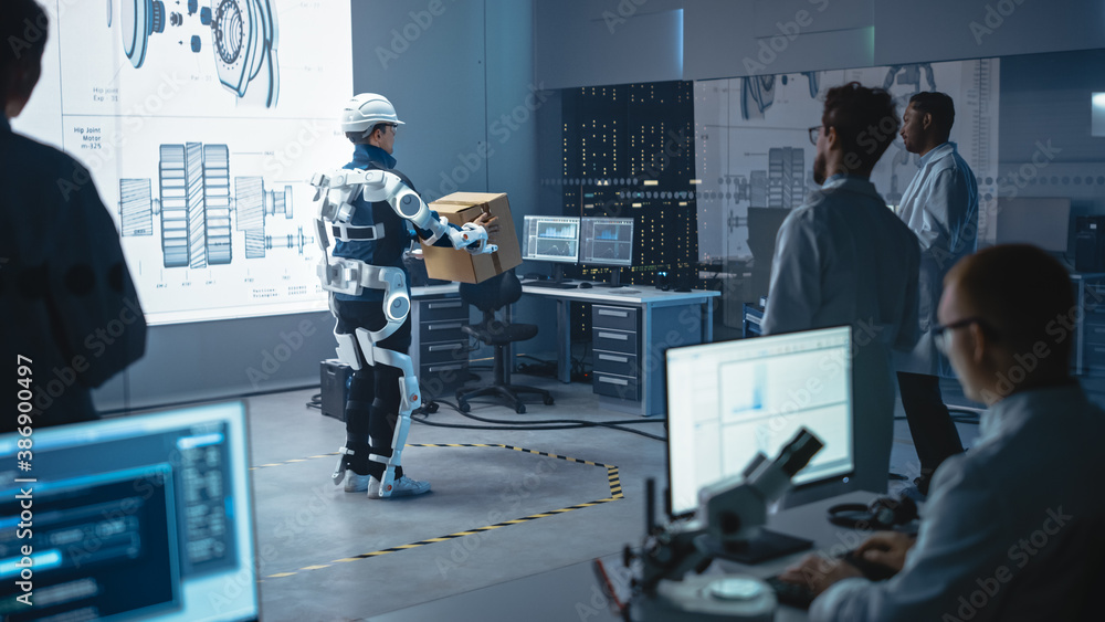 Leinwandbilder In Development Laboratory: Engineers Look at Robotics Exoskeleton Prototype Presentation with Person Testing it, Moving Heavy Carboard Box. Designing Wearable Exosuit to Help Warehouse Workers