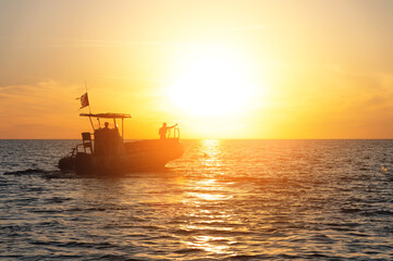 Fototapeta premium Sunset seascape two fishermen on an inflatable boat against the setting sun