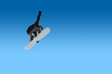 Young woman snowboarder doing snowboard trick in the air with board grab on isolated blue gradient