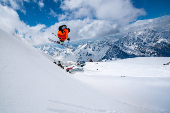 Professional athlete skier freerider in an orange suit with a backpack flies in the air after jumping on the lags on the background of blue snow and mountains