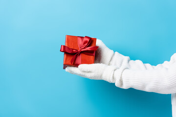 cropped view of young woman in gloves holding gift box on blue
