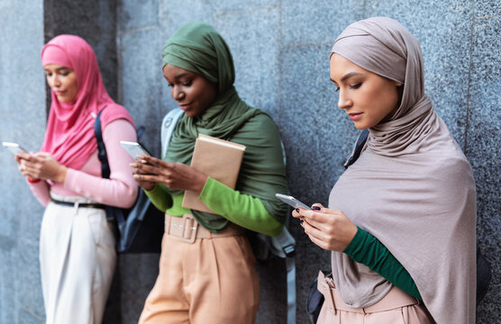 Modern Arab Ladies Using Smartphones Standing Over Gray Wall