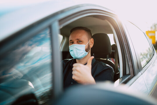 A portrait of a handsome caucasian businessman in a black shirt with a face mask giving a thumbs up while driving a car on the way to work. Protection during the COVID - 19 coronavirus pandemic