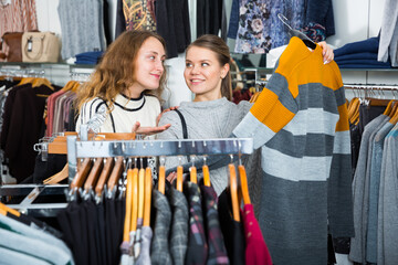 Portrait of two female friends choosing cardigan in clothing shop