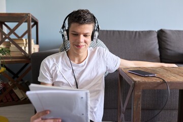 Teenager student in headphones with notebook and smartphone studying
