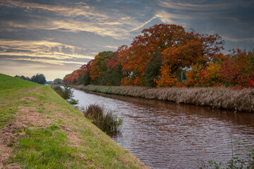 Autumn colors in the trees along the canal and a beautiful colored sky in the Netherlands, Overijssel province
