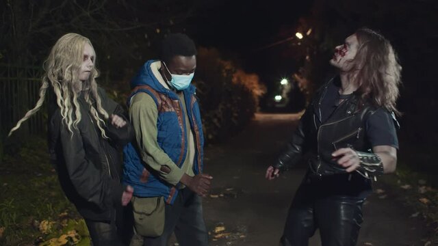 Two zombies and afro man in safety mask dancing on dark street