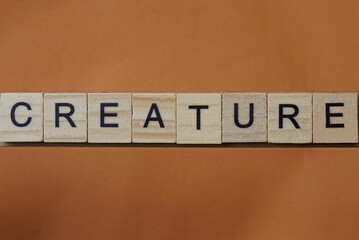 gray word creature made of wooden square letters on brown background