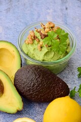 Avocado sauce with walnut and parsley in glass jar. Blue background