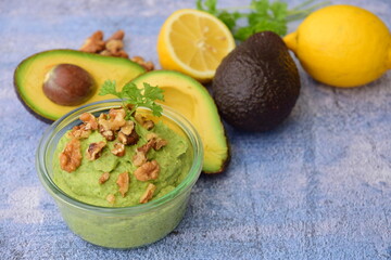 Avocado sauce with walnut and parsley in glass jar. Blue background