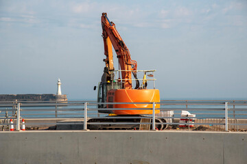 UK. 2020.  Civil engineering work being carried out on a h arbour using a excavator with a backdrop of the harbour entrance.