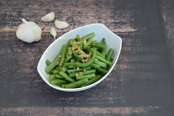Sautéed green beans with garlic in a bowl on wooden background