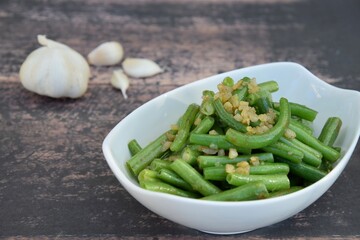 Sautéed green beans with garlic in a bowl on wooden background