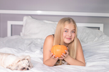 beautiful happy blonde with a pumpkin on bed with white sheets. halloween concept.