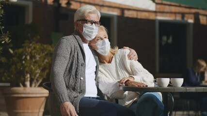 Mature couple in protective mask hugging sitting in street cafe - Powered by Adobe