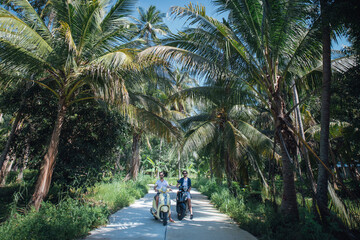 Two men on motorcycles in palm trees on a tropical island